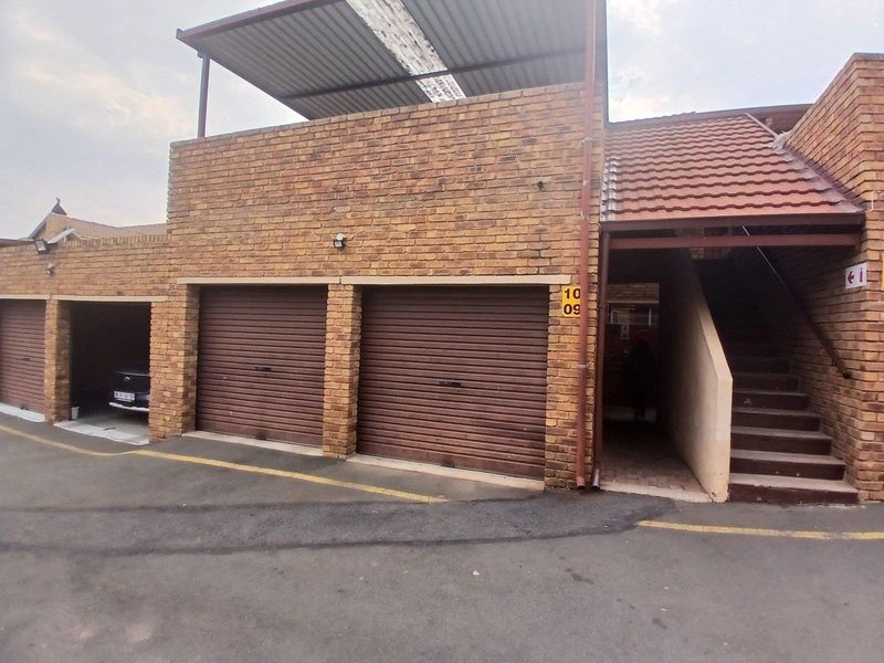 Exterior view of a townhouse complex featuring multiple roller shutter garage doors, a brick facade, and an external staircase leading to an upper level.