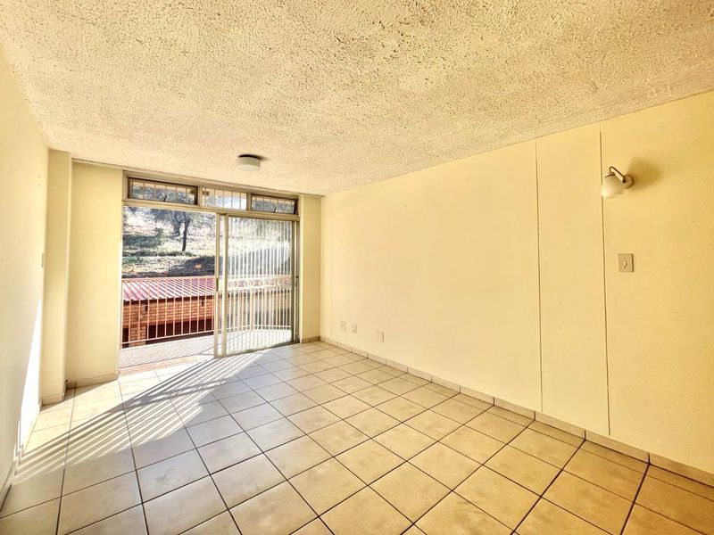 An empty living room featuring ceramic floor tiles, a textured ceiling, and a sliding glass door providing access to an outdoor balcony area.