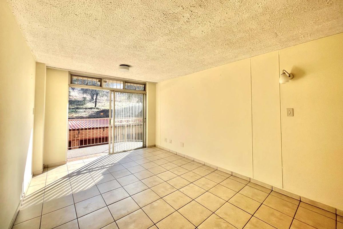 An empty living room featuring ceramic floor tiles, a textured ceiling, and a sliding glass door providing access to an outdoor balcony area.