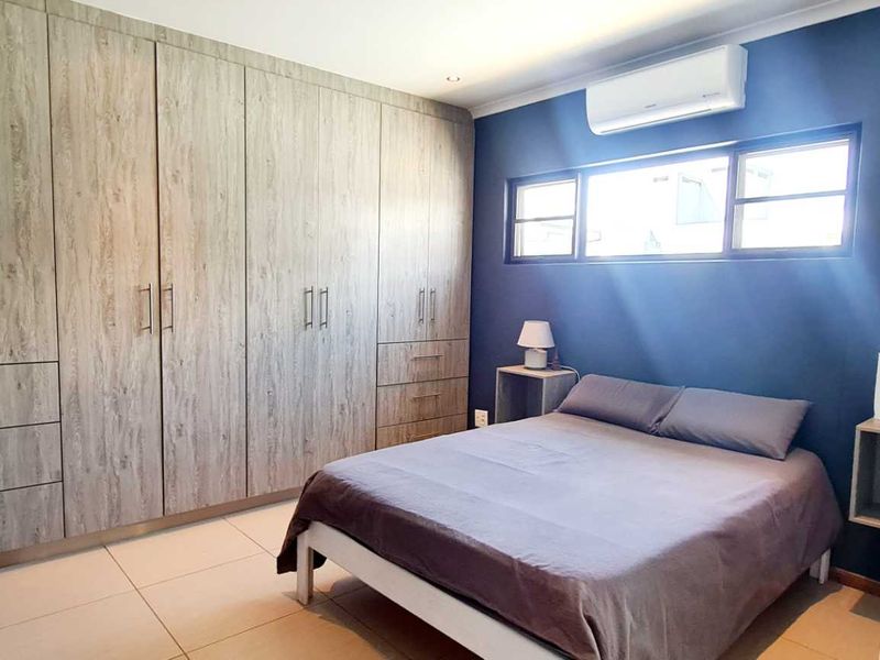A well-maintained bedroom featuring extensive built-in wooden cabinetry, tiled flooring, and a wall-mounted split-system air conditioning unit.