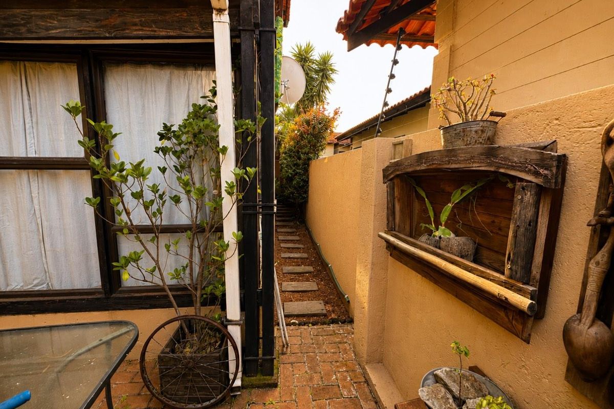 A narrow side passage featuring brick paving, a stepped garden path, and a boundary wall connecting to the rear exterior of the house.