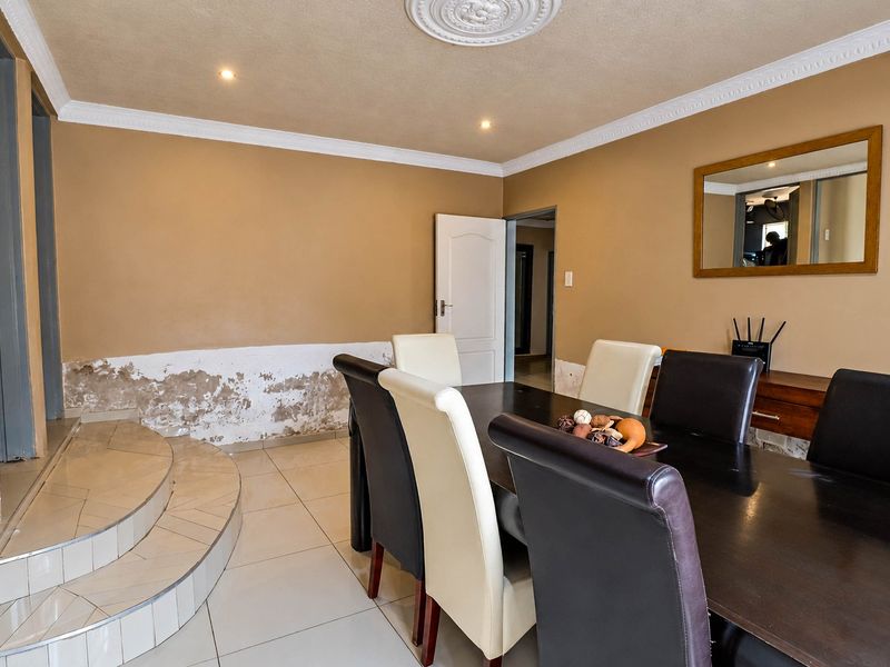 Dining room featuring tiled flooring, a raised platform, and decorative ceiling cornicing. The walls show significant signs of rising damp and require repair.
