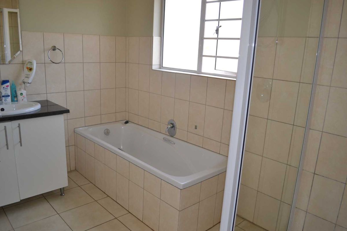 A functional bathroom featuring a built-in vanity, a tiled bathtub, and a separate shower enclosure with neutral wall and floor tiling.