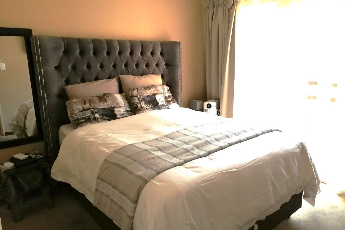 A cozy bedroom featuring neutral wall tones, carpeted flooring, and a large window with curtains allowing for natural light.