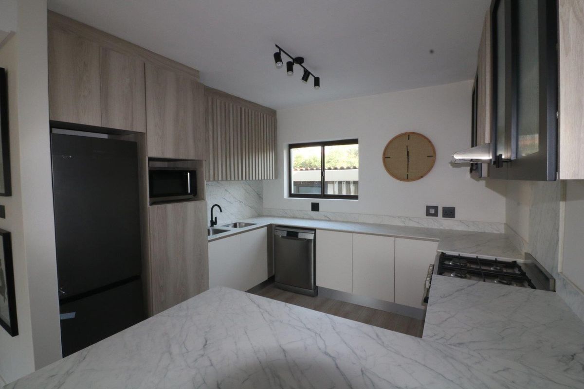 Modern kitchen featuring light wood-tone cabinetry, marble-look countertops, integrated appliances, and a gas hob with an extractor fan.