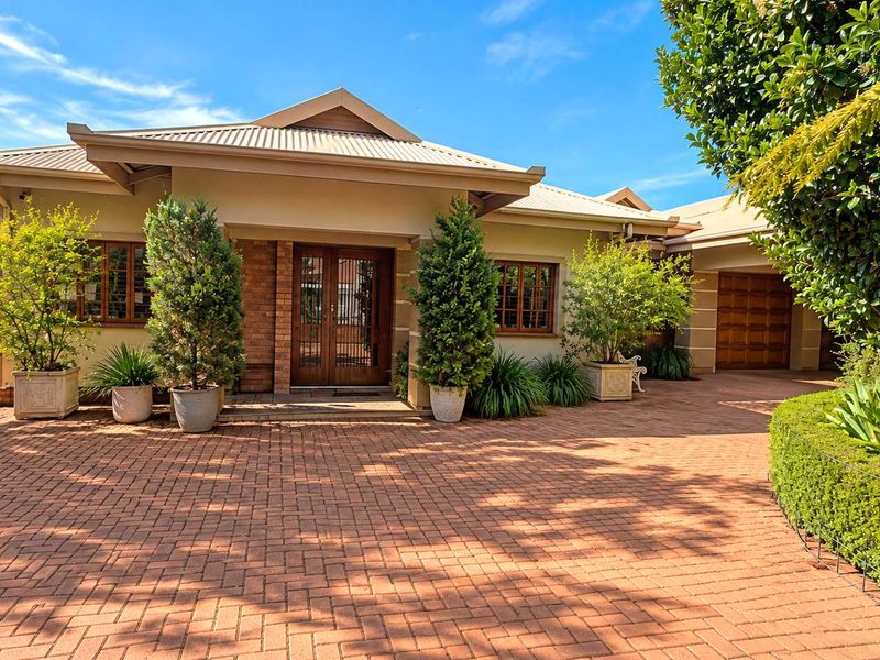 A well-maintained front elevation featuring a brick-paved driveway, timber-framed entrance doors, and a classic brick facade with a corrugated metal roof.