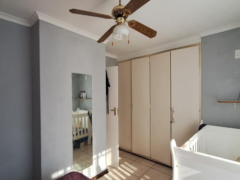 A bedroom featuring built-in cupboards, tiled flooring, and a ceiling fan, offering a functional space with neutral wall tones.