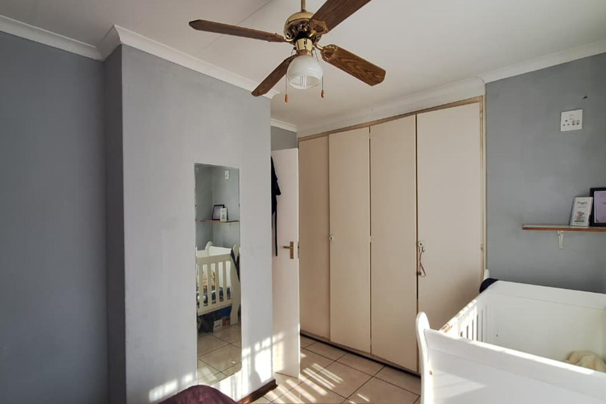 A bedroom featuring built-in cupboards, tiled flooring, and a ceiling fan, offering a functional space with neutral wall tones.