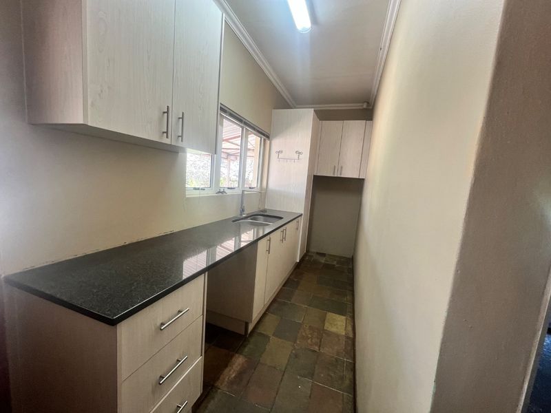 A functional galley-style kitchen featuring light wood-look cabinetry, dark granite countertops, a stainless steel sink, and durable tiled flooring.