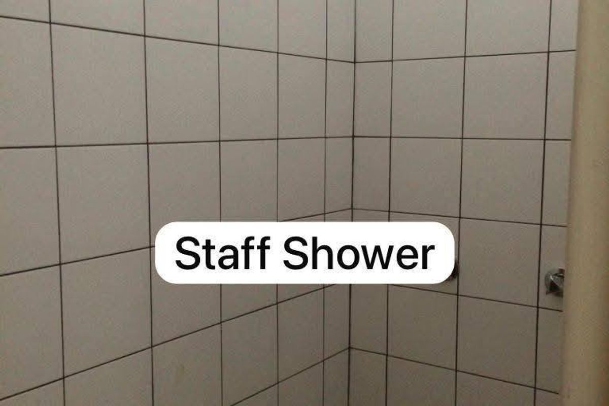 A functional staff shower area featuring white wall tiles and a fixed shower head.