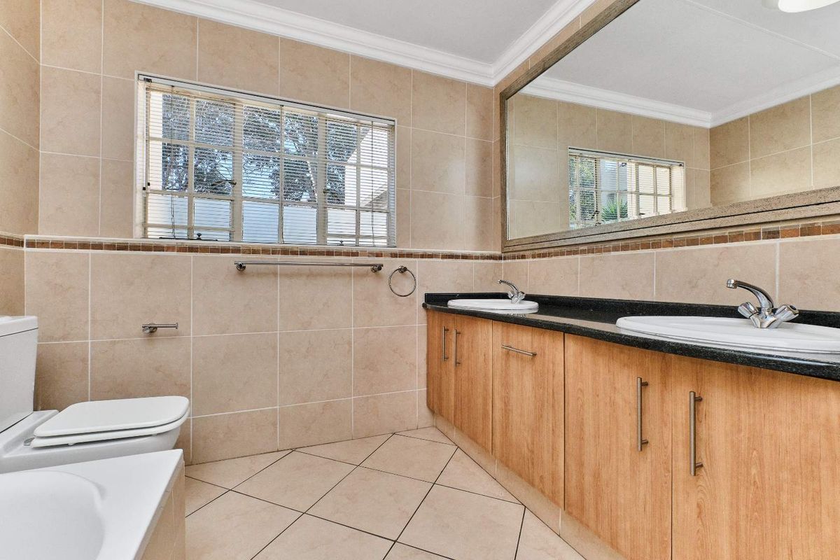 A spacious bathroom featuring a double vanity with granite countertops, large wall mirror, tiled finishes, and a clean, functional layout.