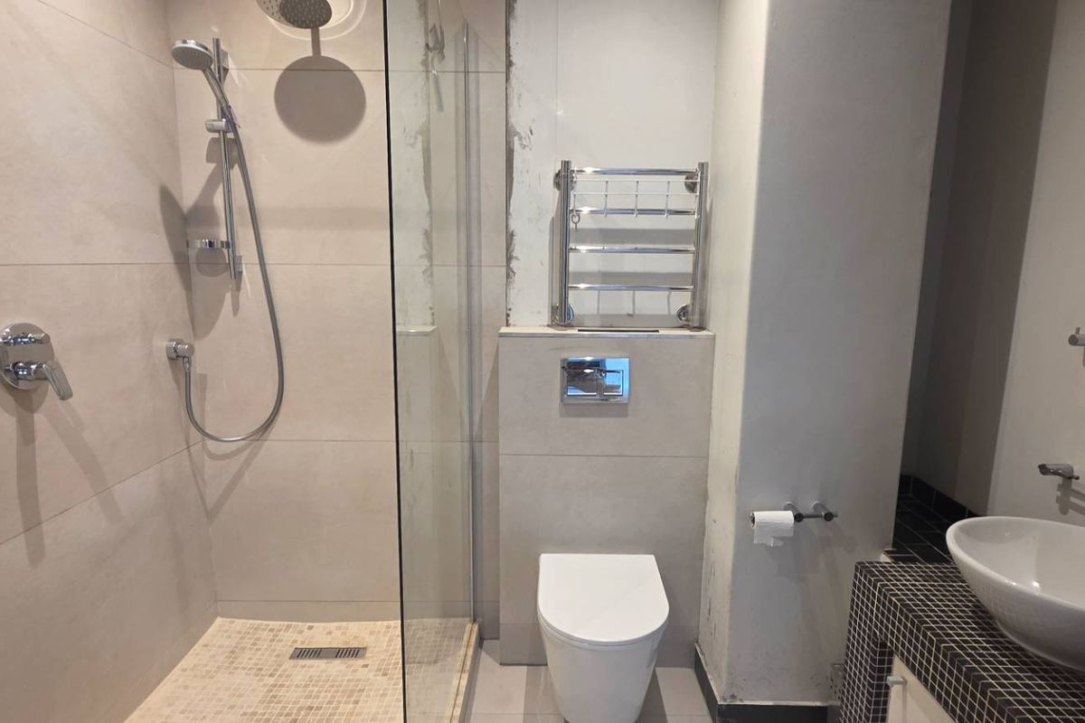 Modern bathroom featuring a walk-in shower with glass screen, wall-mounted toilet, heated towel rail, and a vessel sink on a mosaic-tiled vanity.