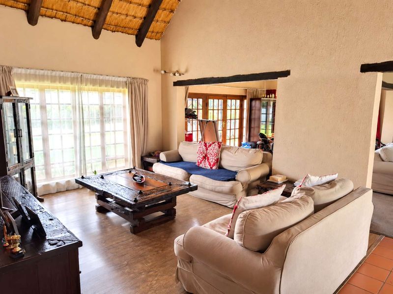 Spacious living room featuring a high vaulted thatched ceiling with exposed timber beams, laminate flooring, and large windows providing natural light.