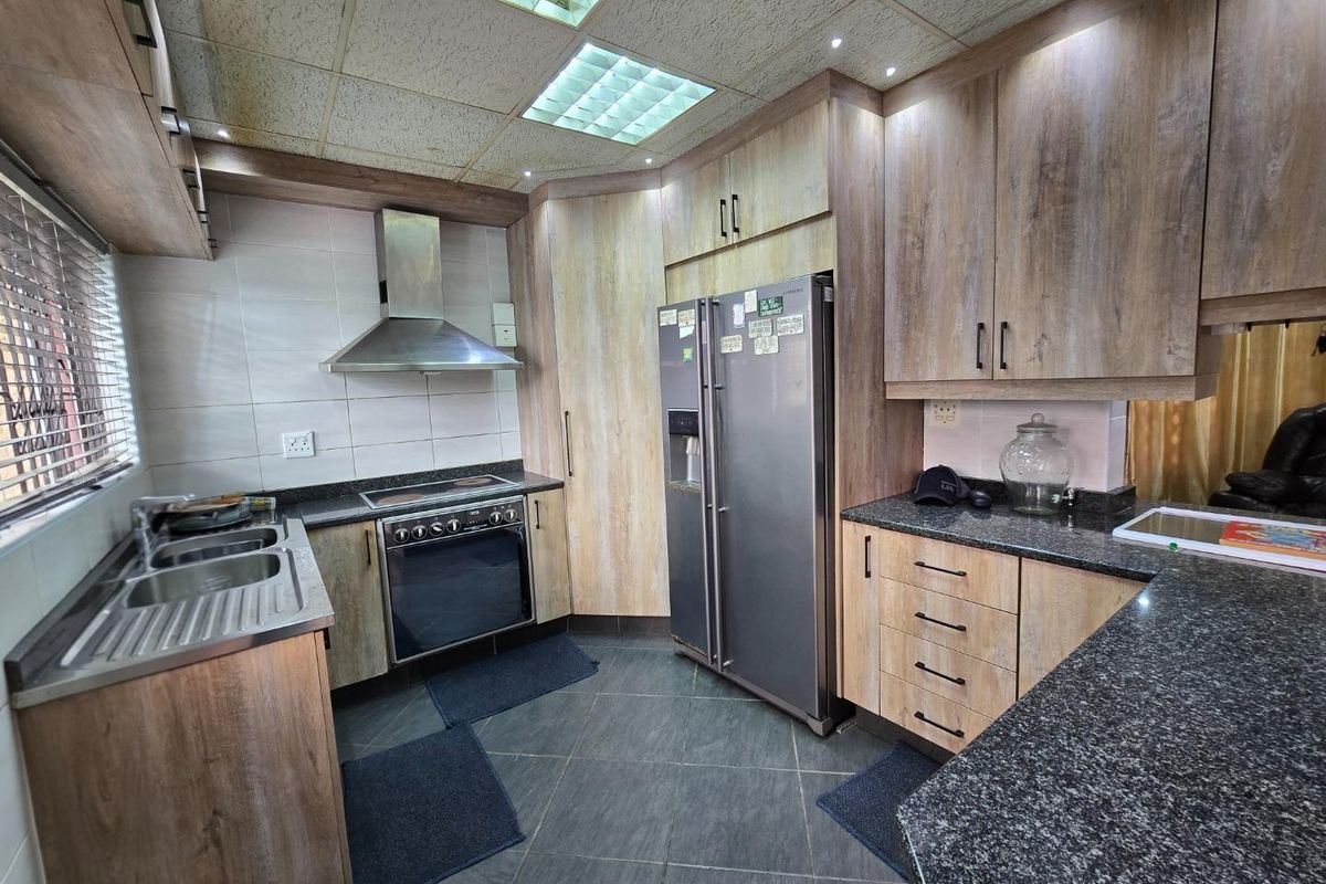 A functional kitchen featuring wood-look cabinetry, granite countertops, a stainless steel extractor fan, and a built-in oven with a tiled floor.