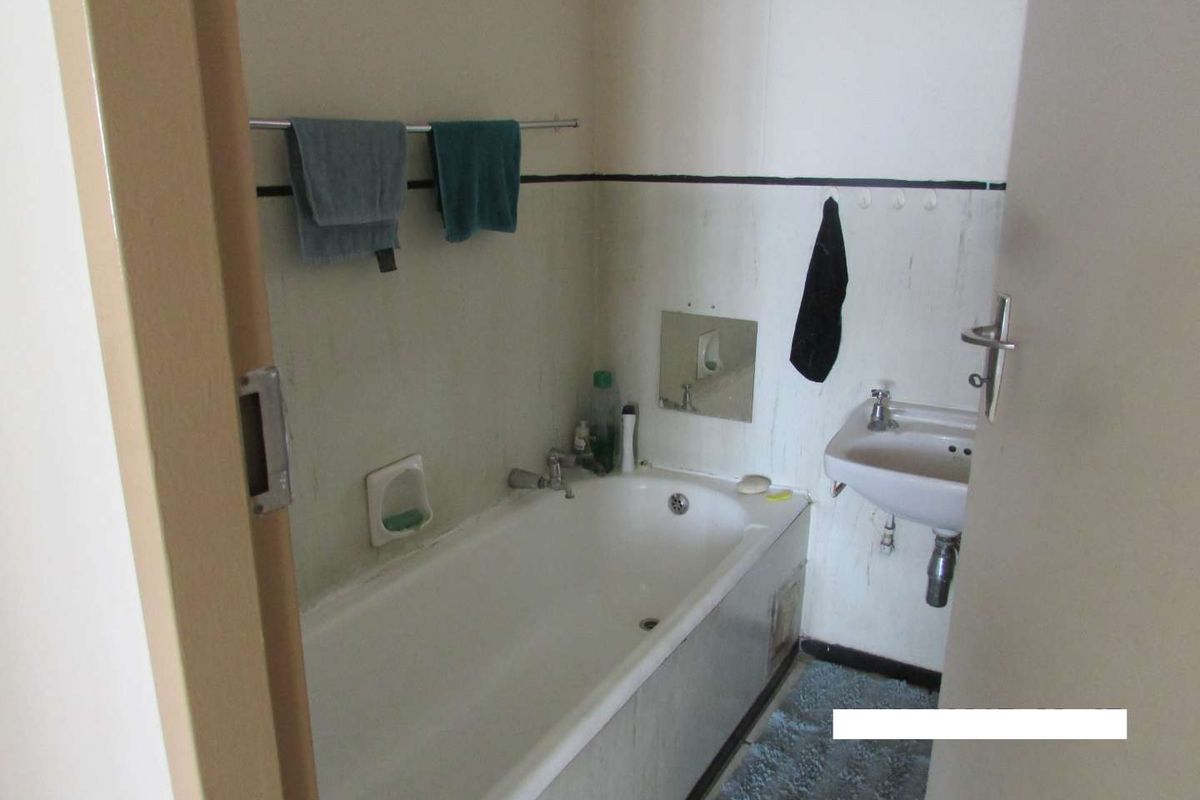 A compact bathroom featuring a standard bathtub and wall-mounted basin, requiring cosmetic updates and surface refinishing to improve its overall condition.
