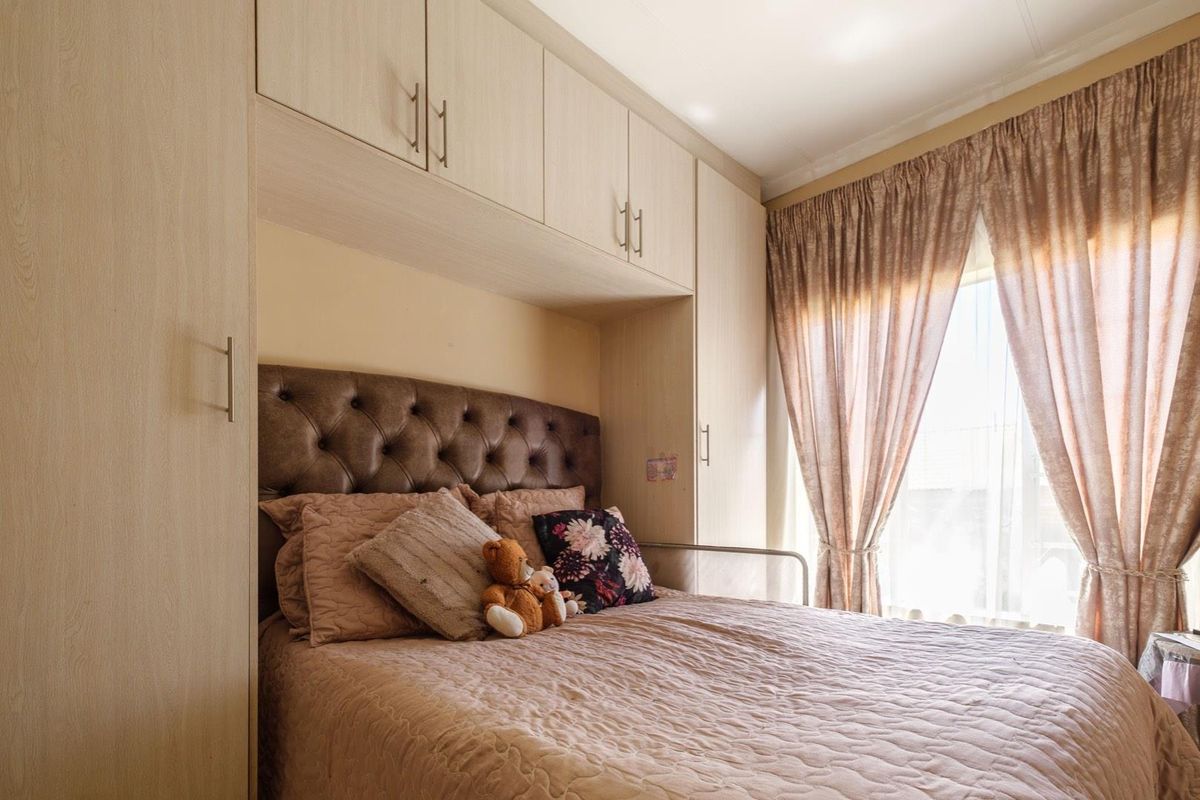 A cozy bedroom featuring built-in light wood cabinetry and overhead storage units, maximizing space efficiency with a functional layout.