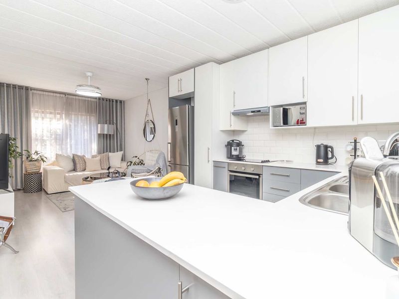 Modern open-plan kitchen and living area featuring sleek cabinetry, subway tile backsplash, integrated appliances, and light laminate flooring.