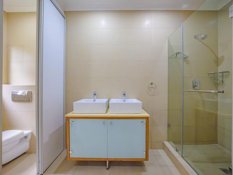 Modern bathroom featuring a double vanity with vessel sinks, a glass-enclosed shower, and a separate wall-mounted toilet with neutral wall tiling.