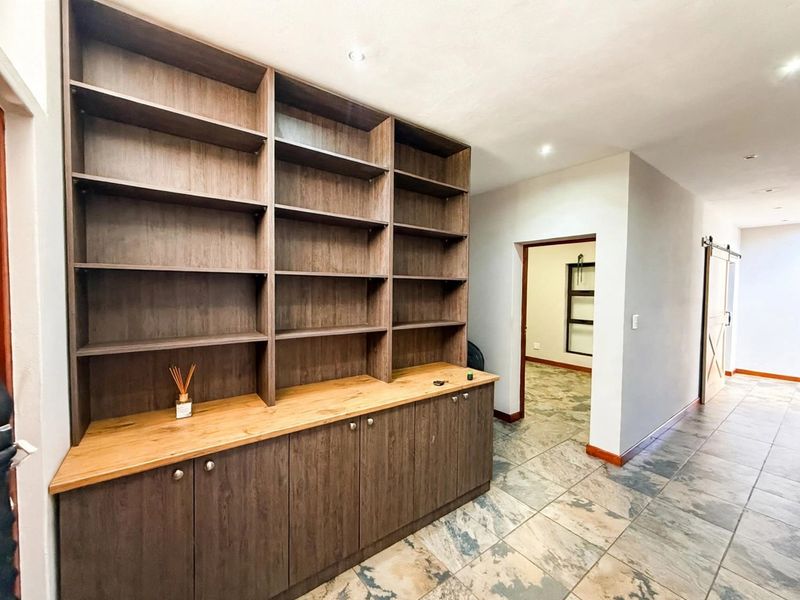A spacious hallway featuring extensive built-in wooden cabinetry with open shelving, stone tile flooring, and a sliding barn door leading to an adjacent room.