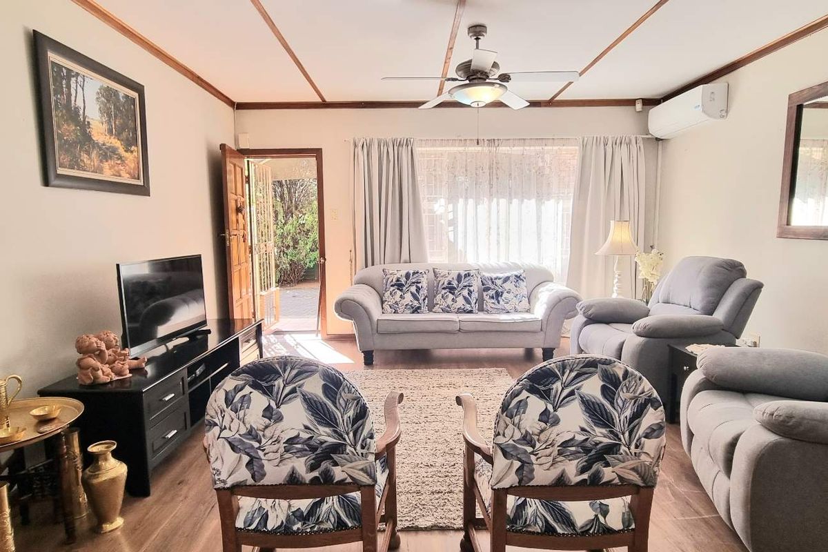 A comfortable living room featuring wood-look flooring, a ceiling fan, and a wall-mounted air conditioning unit, with direct access to the exterior.