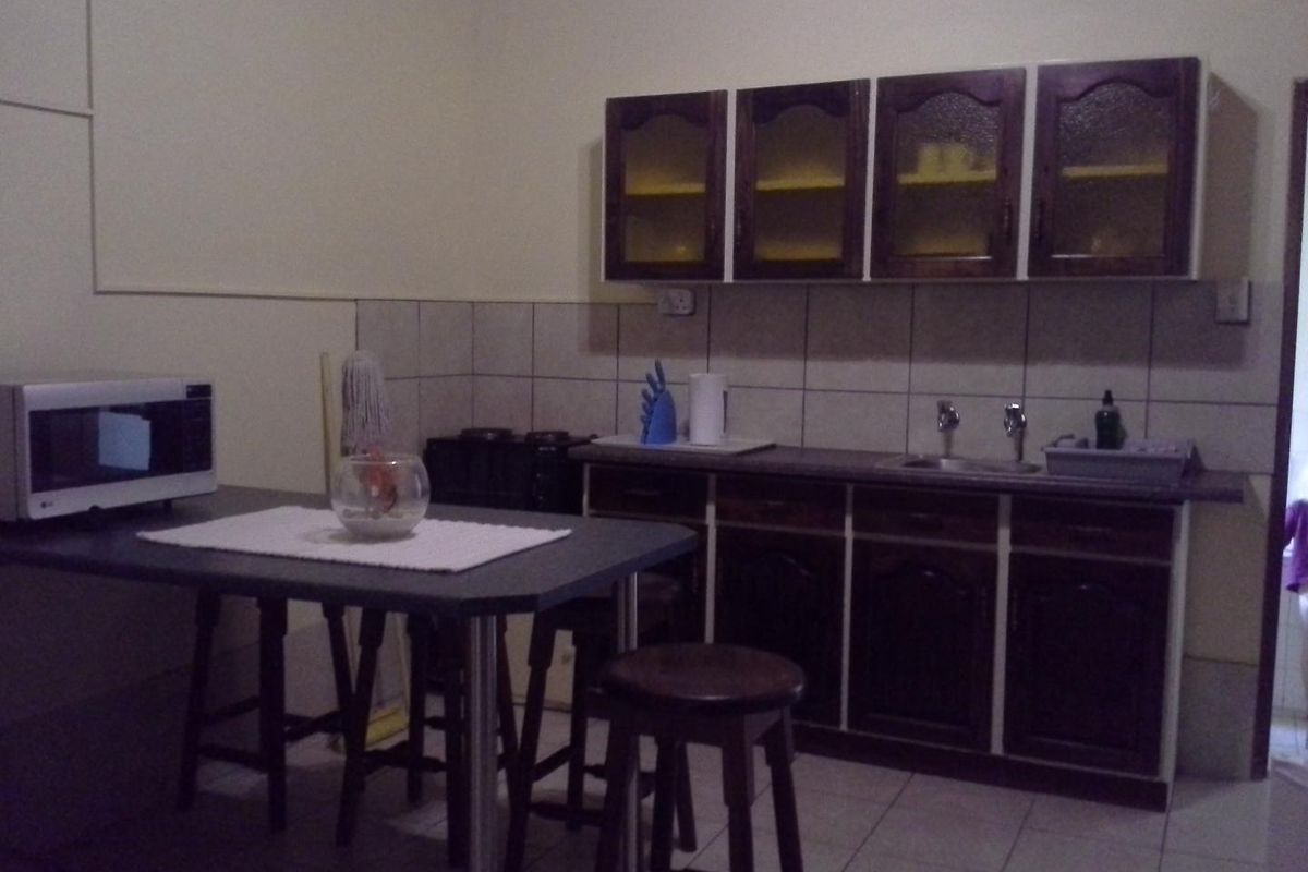 A functional kitchen area featuring dark wood cabinetry, tiled splashbacks, a built-in sink, and a breakfast bar setup.
