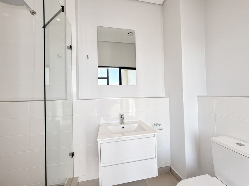 A modern, clean bathroom featuring a glass shower enclosure, wall-mounted vanity with basin, and neutral tiled finishes throughout.