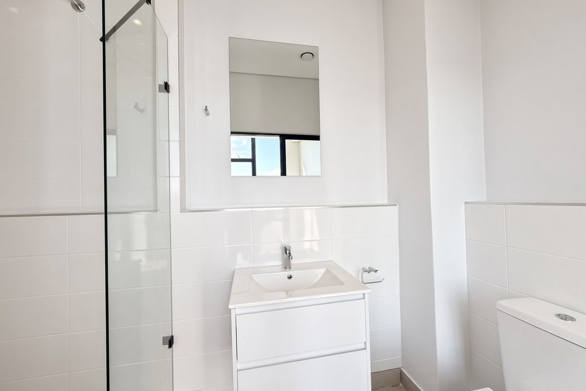 A modern, clean bathroom featuring a glass shower enclosure, wall-mounted vanity with basin, and neutral tiled finishes throughout.