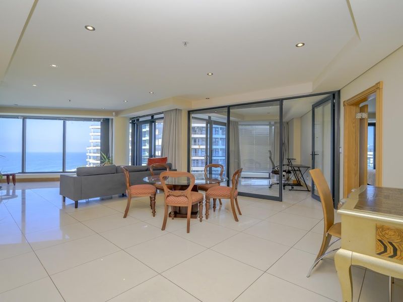 Spacious open-plan living and dining area featuring large floor-to-ceiling windows with ocean views and a modern glass-enclosed study space.