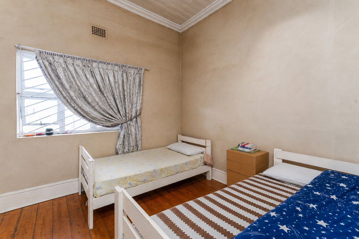 A bedroom featuring original timber flooring, a timber ceiling with cornice detailing, and a window fitted with security bars.