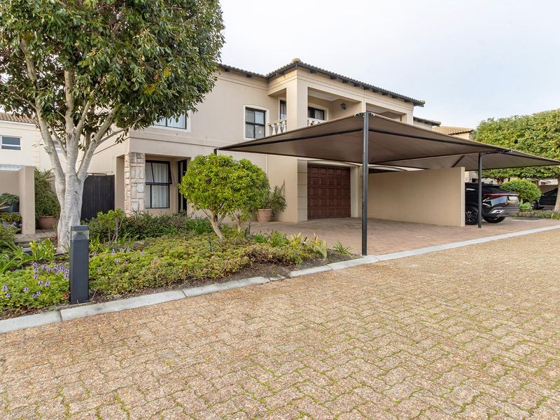 Front elevation of a townhouse featuring a paved driveway, a covered carport, and a garage, complemented by established garden landscaping.