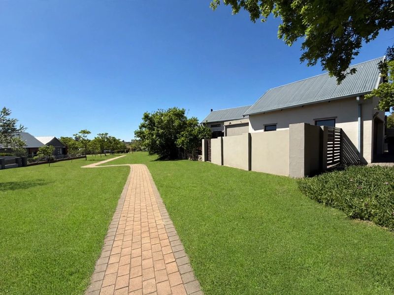 A well-maintained garden area featuring a paved walkway leading through a lush green lawn alongside a modern residential building with a metal roof.