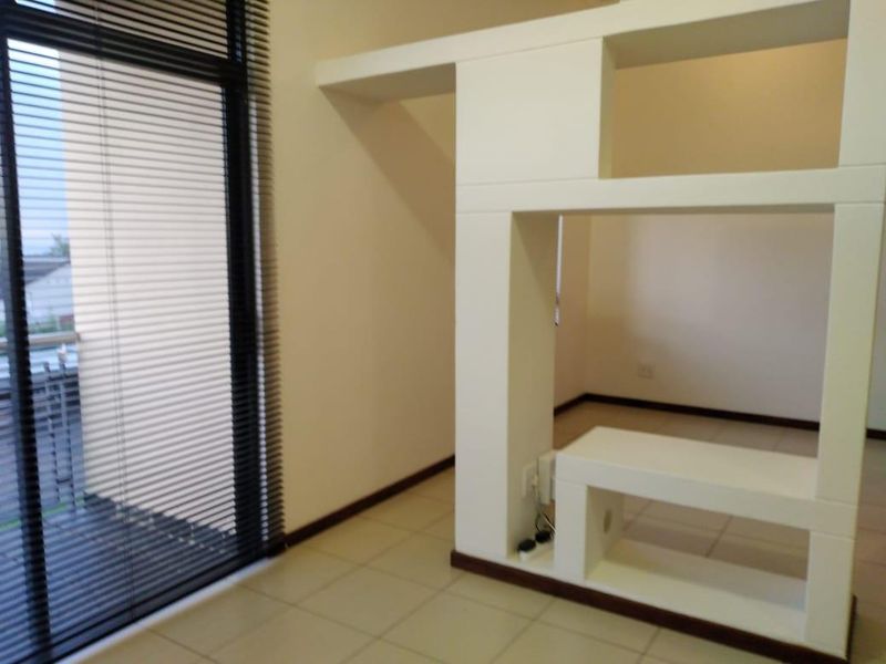 An empty living area featuring tiled flooring, a modern built-in room divider, and a sliding glass door with venetian blinds.
