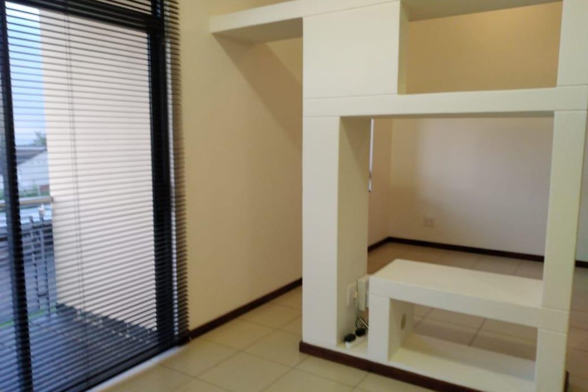 An empty living area featuring tiled flooring, a modern built-in room divider, and a sliding glass door with venetian blinds.