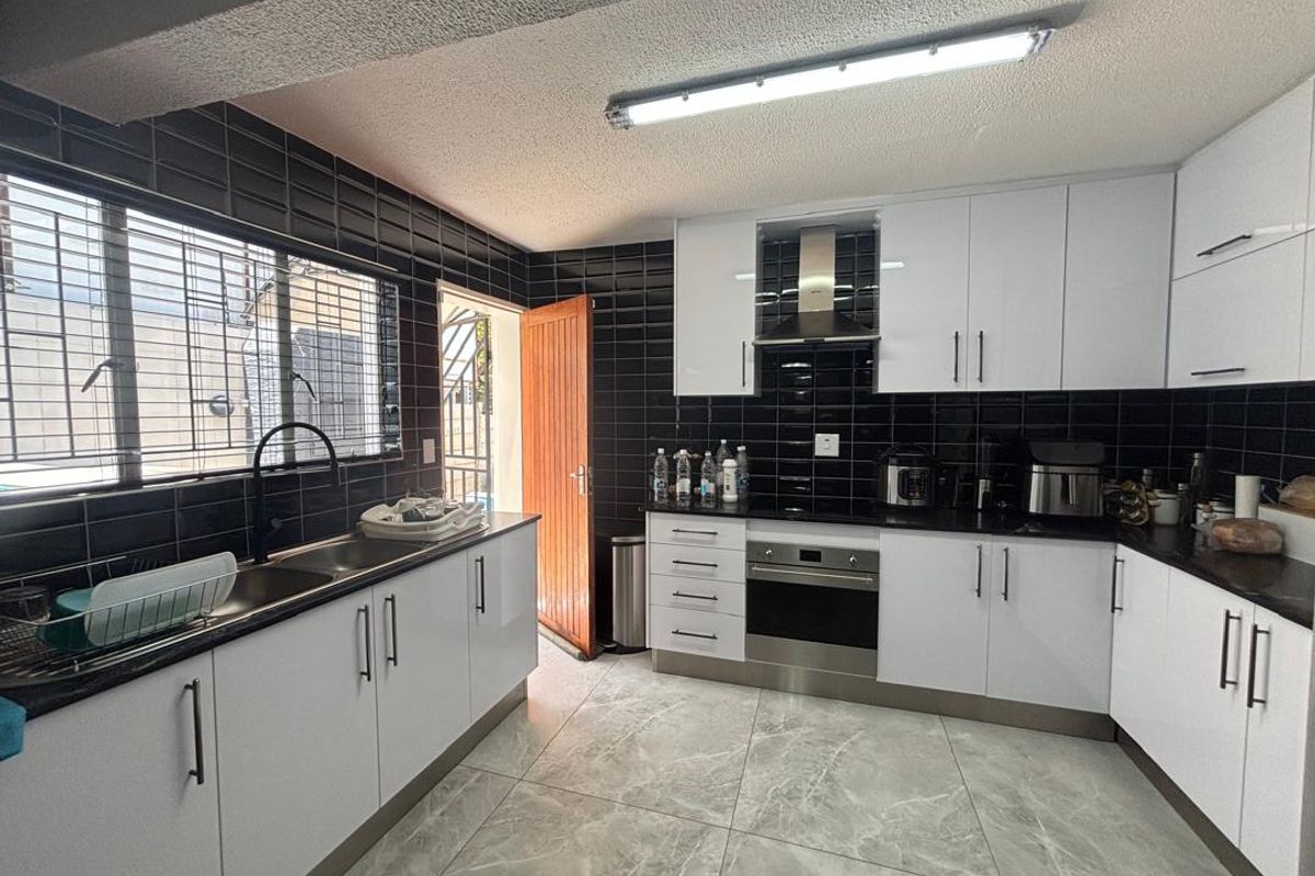 Modern kitchen featuring white cabinetry, contrasting black subway tile backsplash, dark countertops, stainless steel oven, extractor fan, and large format marble-look floor tiles.