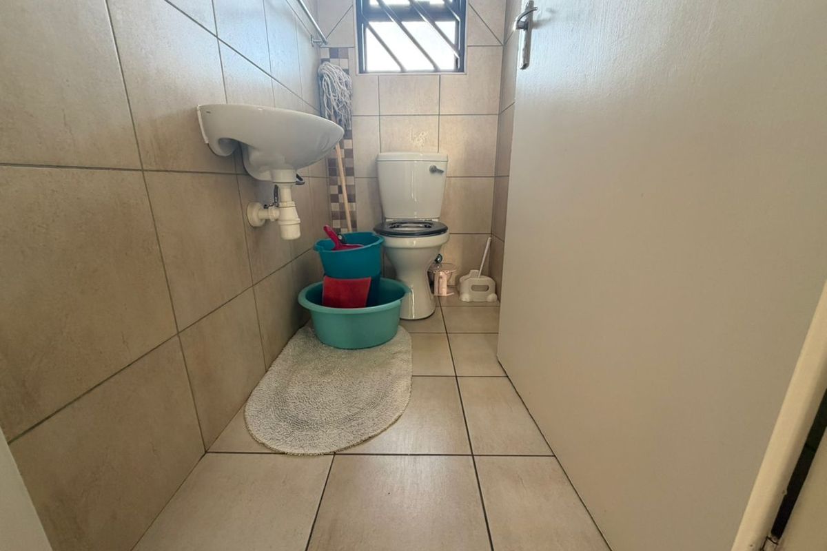 A compact guest bathroom featuring floor-to-ceiling wall tiles, a wall-mounted basin, and a standard toilet with a security-barred window.
