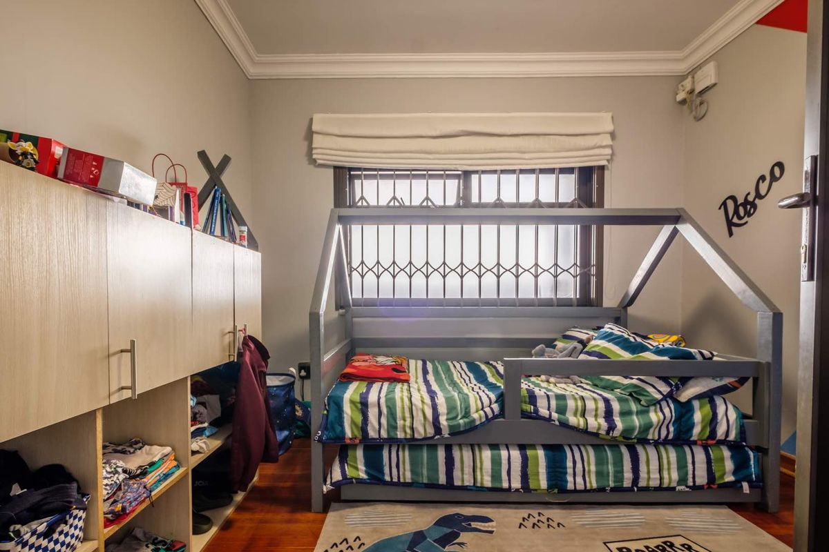 A bedroom featuring built-in cabinetry, crown molding, and a window fitted with security bars and a roman blind.