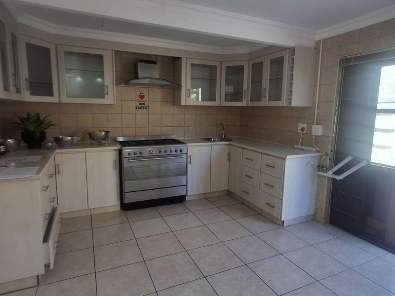 Functional kitchen featuring light-toned cabinetry, stainless steel stove with extractor fan, tiled backsplash, and direct access to an outdoor area.
