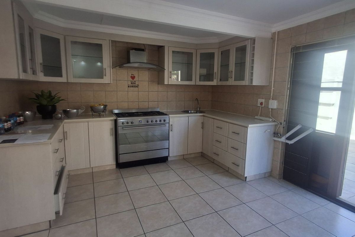 Functional kitchen featuring light-toned cabinetry, stainless steel stove with extractor fan, tiled backsplash, and direct access to an outdoor area.