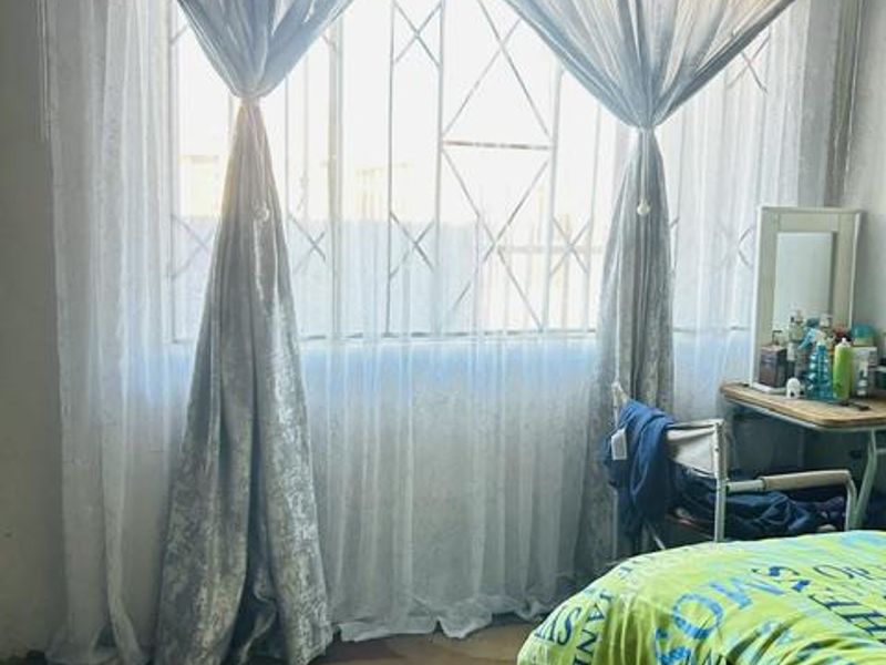 A bedroom featuring a large window with installed security bars, providing natural light and ventilation.