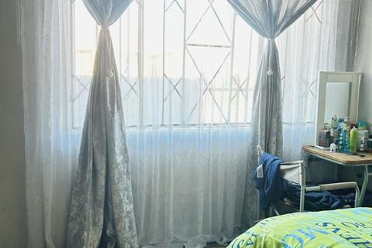 A bedroom featuring a large window with installed security bars, providing natural light and ventilation.