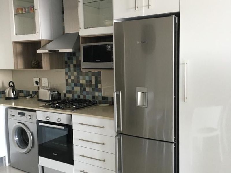 Modern kitchen featuring white high-gloss cabinetry, stone countertops, mosaic tile backsplash, and integrated stainless steel appliances including a gas hob and oven.