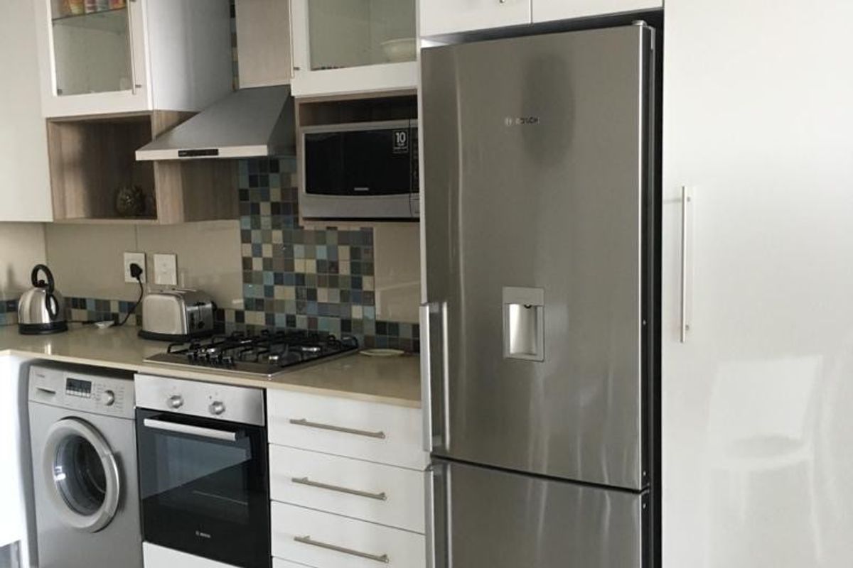 Modern kitchen featuring white high-gloss cabinetry, stone countertops, mosaic tile backsplash, and integrated stainless steel appliances including a gas hob and oven.