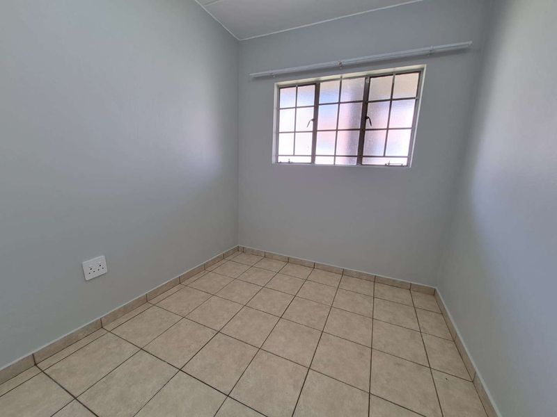 A clean, empty bedroom featuring neutral wall paint, tiled flooring, and a grid-pattern window, providing a versatile space ready for personalization.
