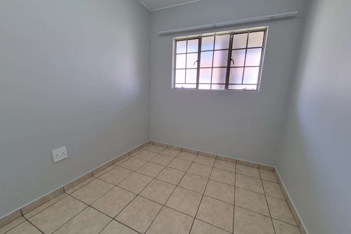 A clean, empty bedroom featuring neutral wall paint, tiled flooring, and a grid-pattern window, providing a versatile space ready for personalization.