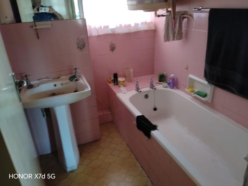 A dated bathroom featuring pink wall tiles, a pedestal basin, and a built-in bathtub, requiring modernization of finishes and fixtures.