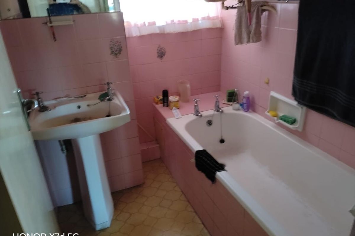 A dated bathroom featuring pink wall tiles, a pedestal basin, and a built-in bathtub, requiring modernization of finishes and fixtures.