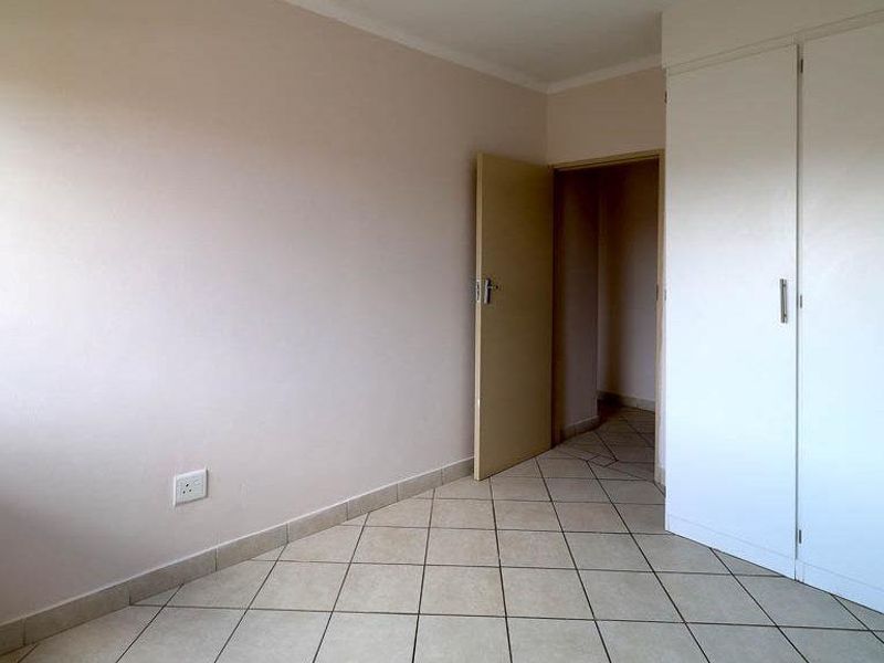 A clean, empty bedroom featuring neutral wall paint, tiled flooring, and built-in storage cupboards.