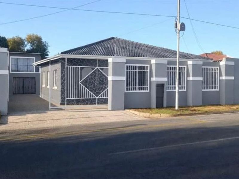 Front elevation of a well-maintained house featuring a tiled roof, paved driveway, secure boundary wall, and fitted security bars on windows.