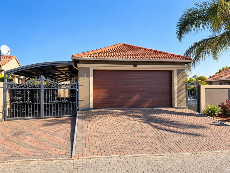 Front view of the property featuring a paved driveway, automated garage door, secure wrought iron gate, and a covered carport area.