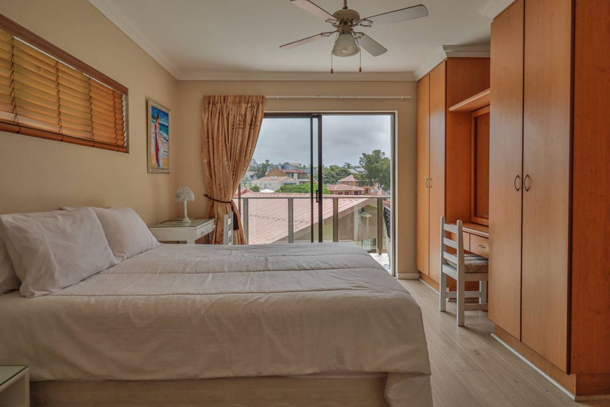A well-lit bedroom featuring built-in wooden cabinetry, a ceiling fan, and sliding glass doors that open onto a private balcony with neighborhood views.